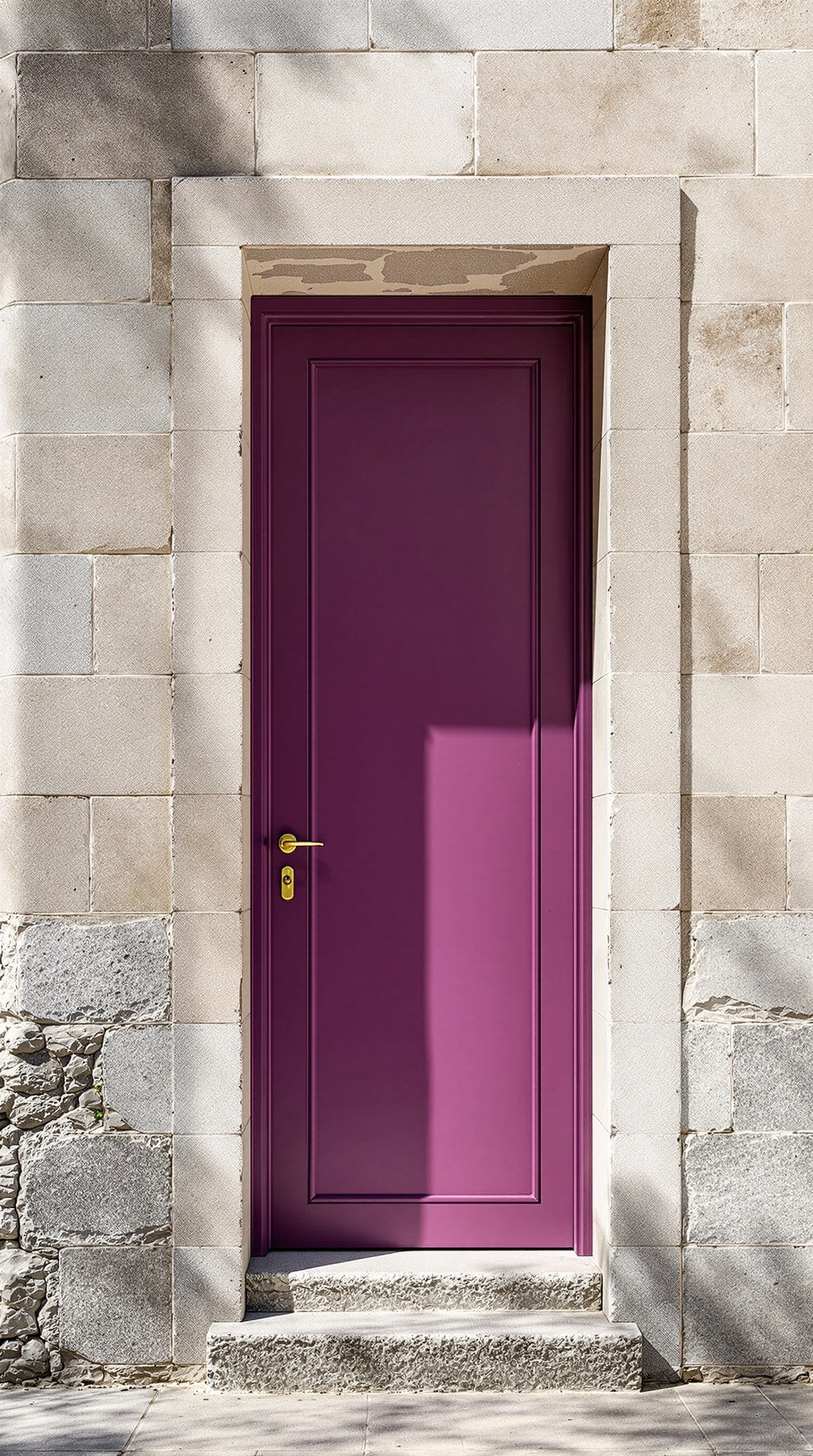 A narrow aubergine-painted door sits inset within a thick frame of bleached limestone blocks, brass handle catching warm sun. Hard midday light slants across the facade, throwing a crisp diagonal shadow over the door's face and chalky masonry. Mediterranean stillness, color-block geometry, shot on a sharp 35mm prime with rich saturated tonality.