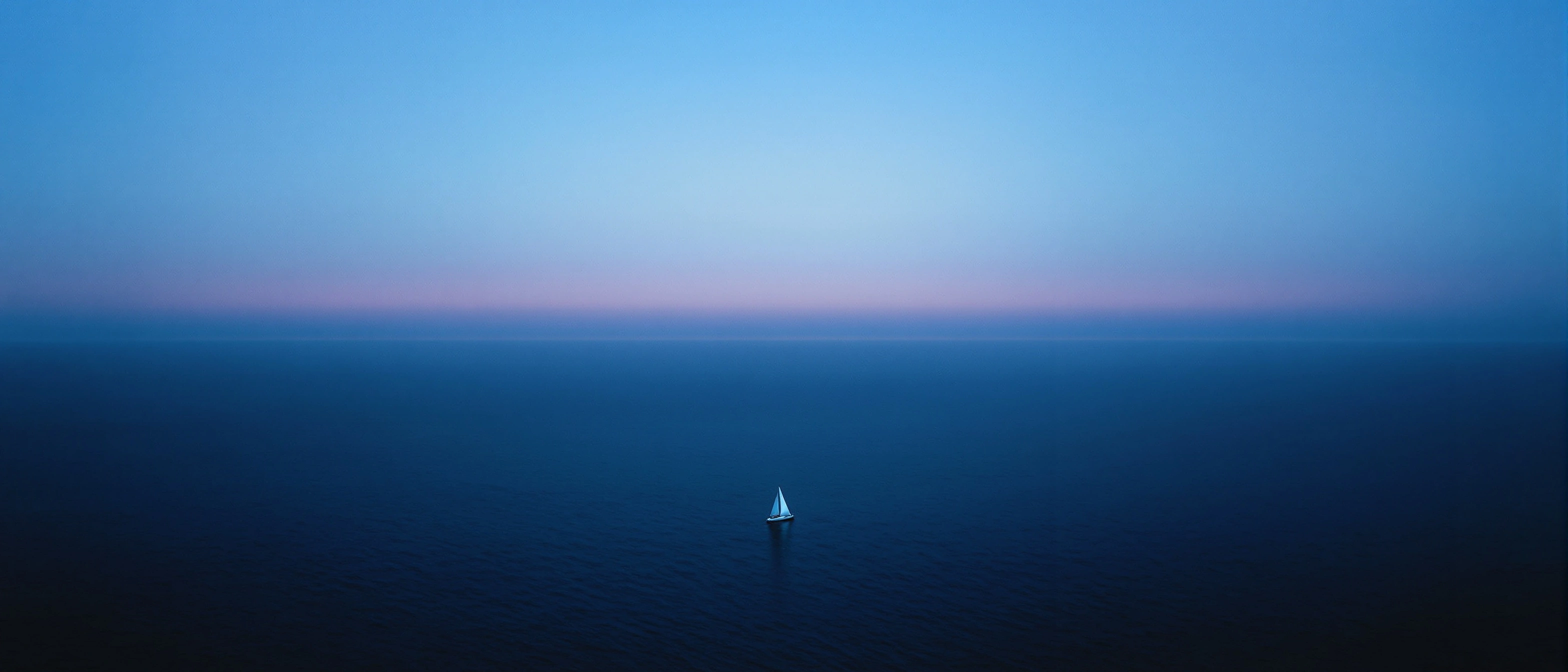 Letterbox seascape at dusk, a slate ocean stretched flat to a faint horizon where a single white sailboat hovers under a band of dusty pink. Above, ultramarine deepens upward into night sky. Minimalist, contemplative, large-format calm, anamorphic crop.