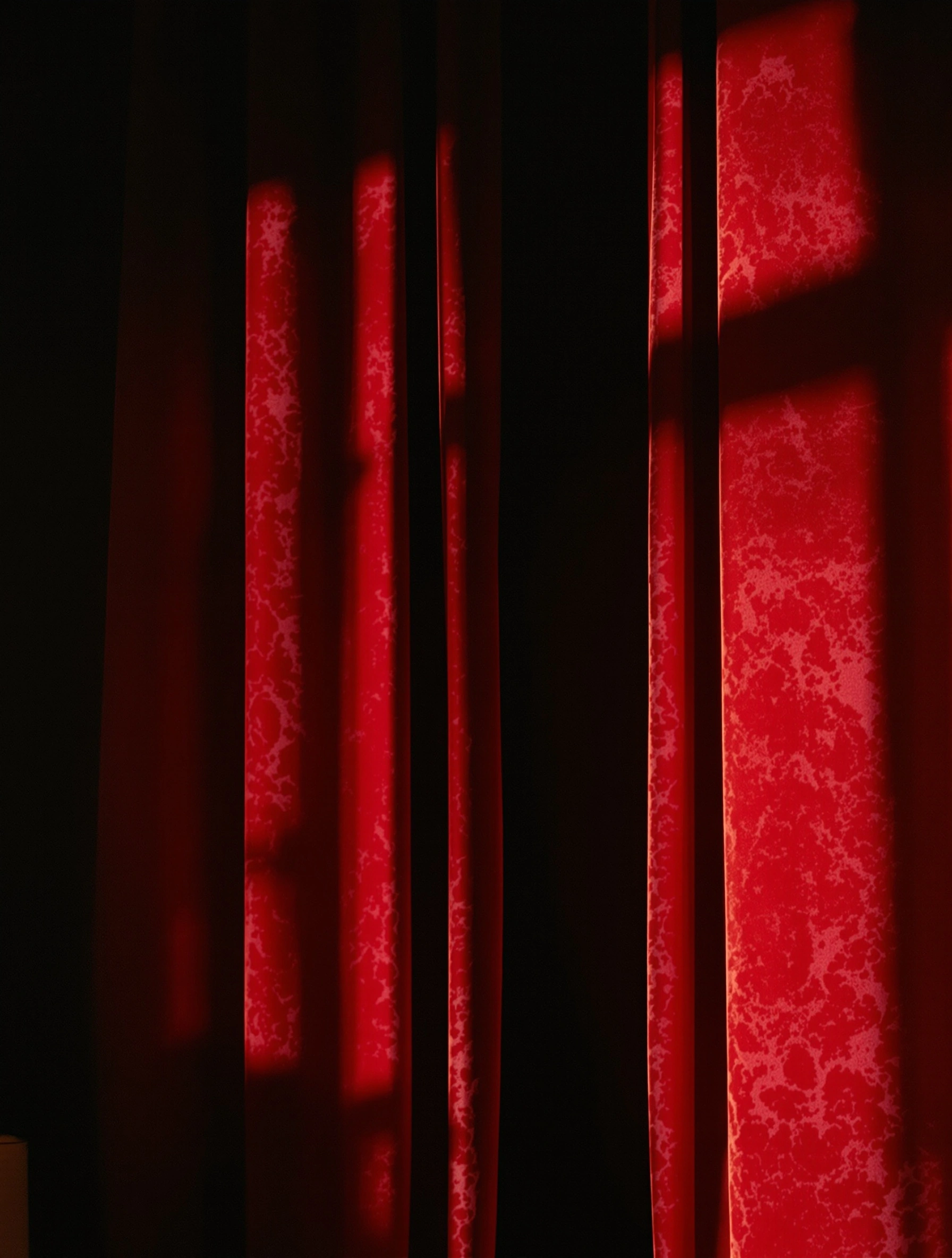 Heavy crushed-velvet drapery in oxblood red catches a single shaft of low sun, the window's mullions printed sharply across the marbled pile while inky shadow swallows the centre fold. Tight vertical crop, near-black negative space, theatrical and operatic, rendered with the dense grain of pushed CineStill 800.