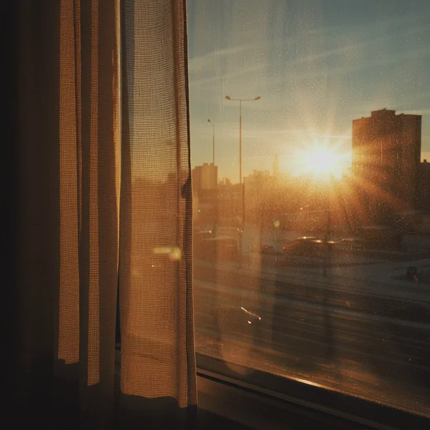 Warm morning sun bursts through a gauzy curtain at a city window, starburst flares scattering across the dusty glass. Distant buildings catch amber light. Quiet, nostalgic, golden-hour wake-up mood. Motion: curtain breathes in the breeze, sunbeams shift across glass, dust motes float through light.